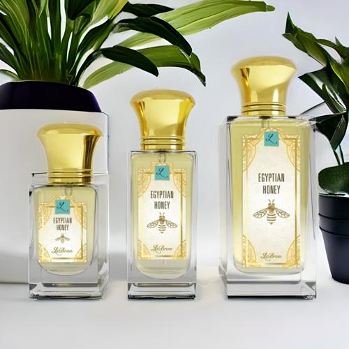 Three sizes of the Egyptian Honey fragrances laid out in a line that shows all their sizes. The label shows a a gold egyptian-style bee with a white background and plant background with "Labron" on their label.