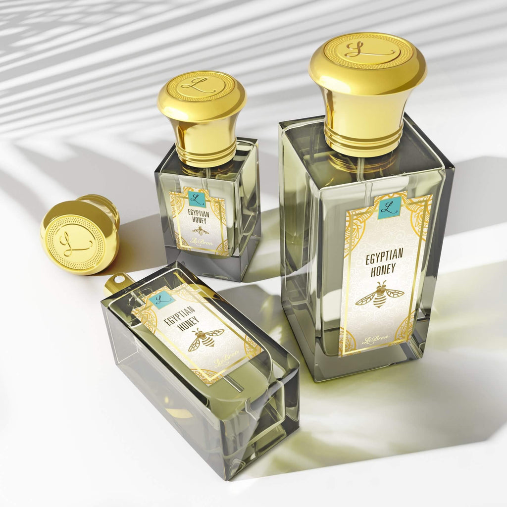 Three sizes of the Egyptian Honey fragrances laid out in a triangle formation with the camera shot in a higher angle to show the shadows of the products. The label shows a a gold egyptian-style bee with a white background with "Labron" on their label.