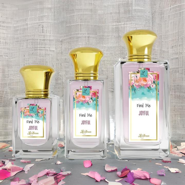 Find me "Joyful" products showcased in a line. This products shows a floral like background on their label and gold cap. The background of the image is surrounded by pink petals and white mesh background..