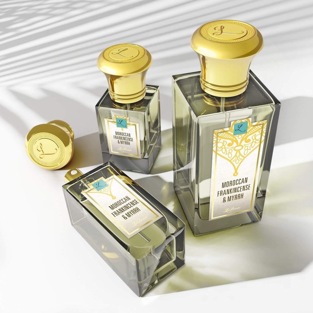 Three sizes of the Moroccan Frankincense & Myrrh perfume laid out in a triangle formation with the camera shot in a higher angle to show the shadows of the products. The label shows a white & gold moroccan style with a white background with "Labron" on their label.