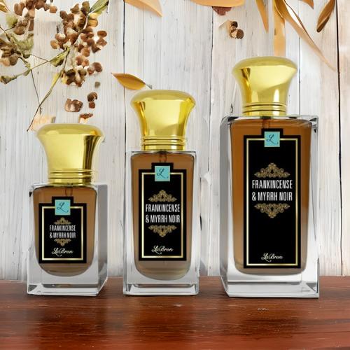 Frankincense & Myrrh products lined up in a formation from smallest to biggest and with a background of woody, brown leaves and a wooden bottom.