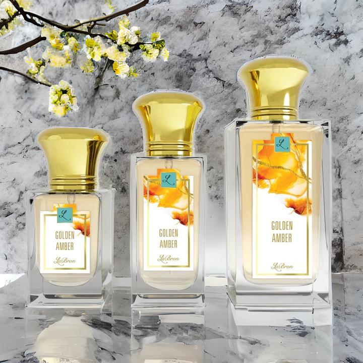 Golden Amber products showcased in a line from smallest to biggest, left to right. This products shows a honey like background on their label and gold cap. The background of the image is surrounded by silver, marble setting with yellow flowers.