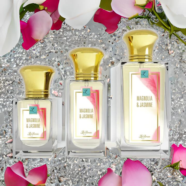 Magnolia & Jasmine Perfume bottles in the standard 1.0 - 3.4 oz lined up with a white background. The magonlia & Jasmine label look is a pink and floral, pink and white background look with gold lettering for the product name. The background seems to be covered in jewels.