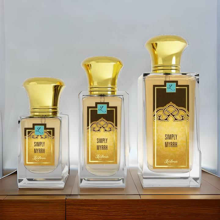 Three bottles of the Simply Myrrh products shown that are 1.0 - 3.4 oz lined up from smallest to biggest. Their label captivates a gold and black moroccan style to the label. The background is is white but the products are set on a wooden desk.