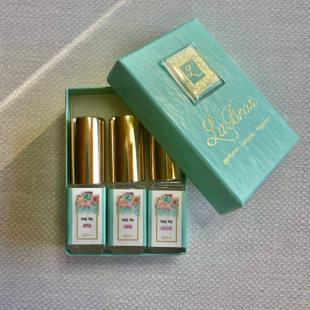 LaBron Perfume "Find Me" Sample Set; with your choice of Three or Six 5 ml Sprays. The box that comes with the products are in a white box with gold lettering for the label. The background is a mesh white look that brings it all together.